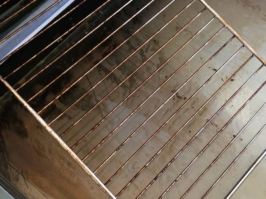 Oven rack and door glass with built-up grime before cleaning